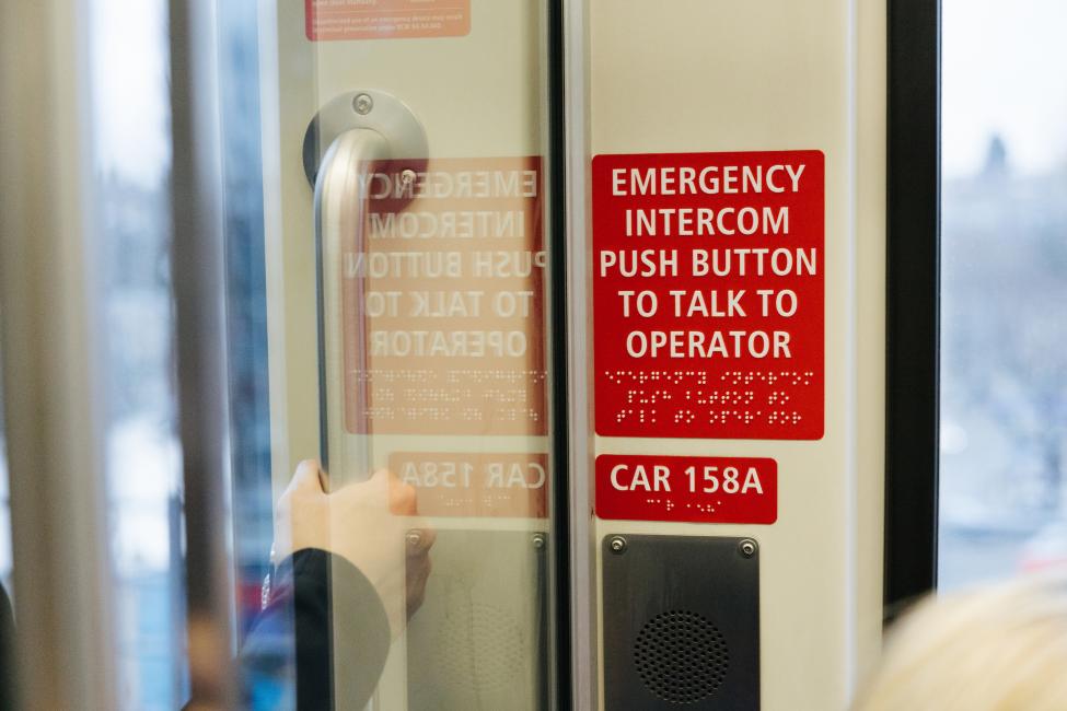 A red sign on the inside of Sound Transit light rail vehicles tells riders how to request assistance by pressing a button to talk to the operator.