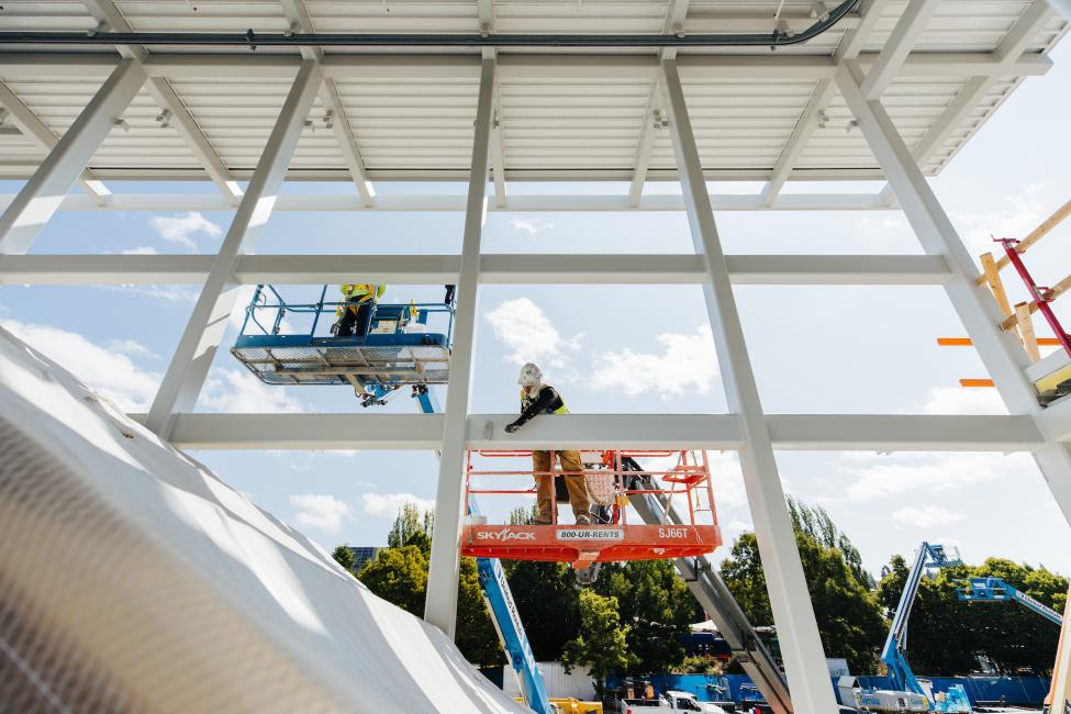 Two workers in lifts examine a structure at Northgate Station.