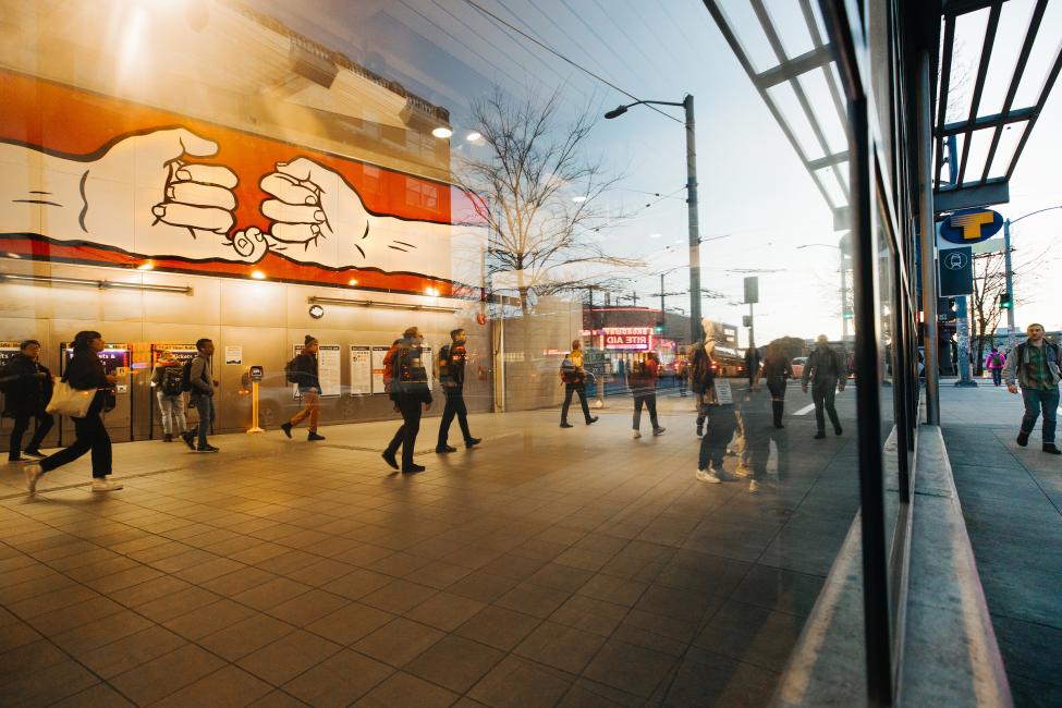 Looking into the entrance of Capitol Hill Station at a mural of two hands, pinkies linked, on the wall above ticket machines and signs.