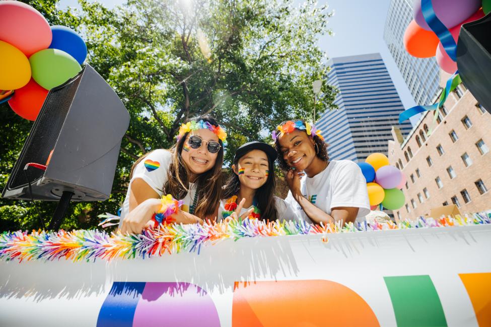 Three people smile from a float in Seattle's Pride Parade on a sunny day.