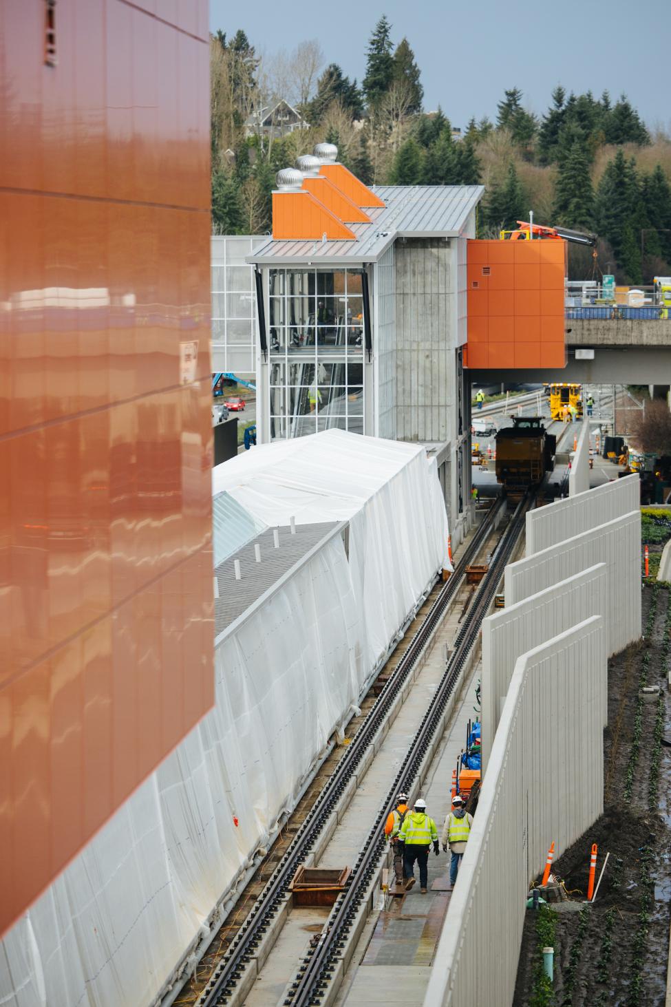 The south headhouse of Mercer Island Station can be seen, as well as some of the tracks and the platform, covered by plastic tarps.