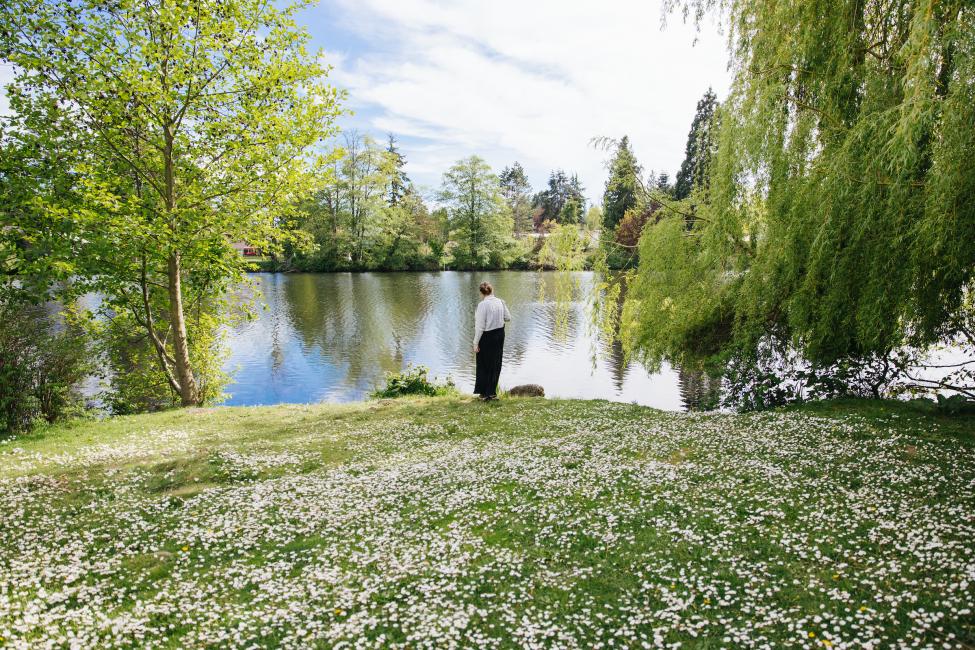 A woman walks through Ronald Bog Park by the water on a sunny day.