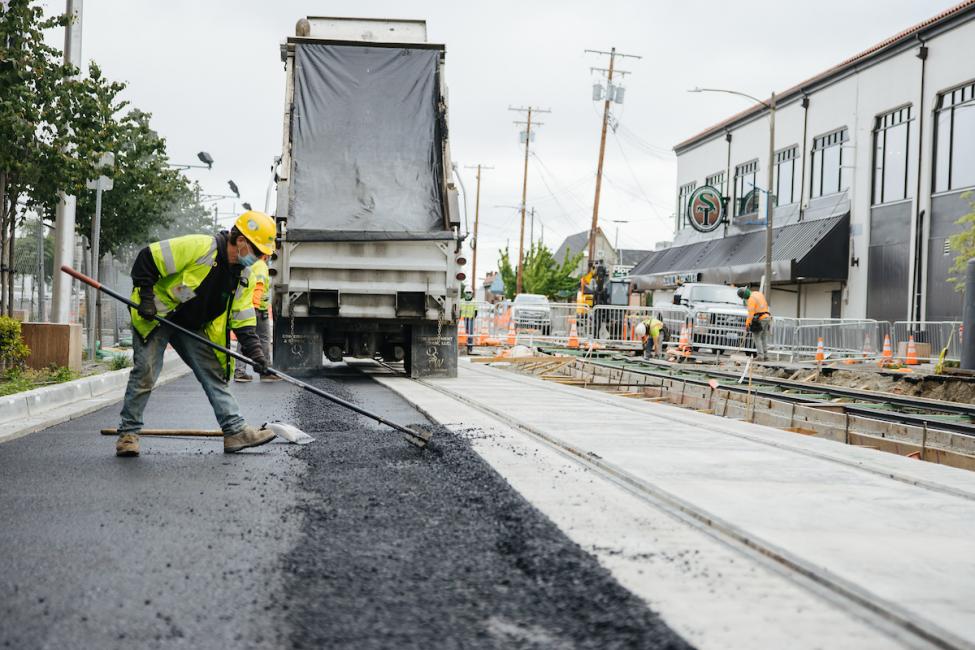 A worker in a hard hat and yellow vest smooths concrete. 