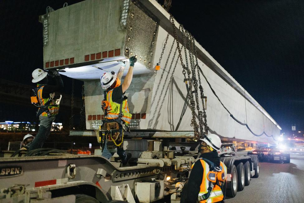 Construction crew members stand on a truck and look at a big concrete structure.