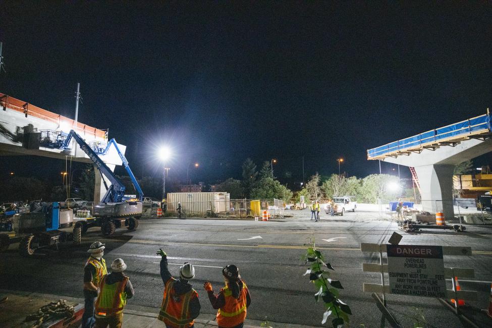 Construction crew members point at a large concrete girder.
