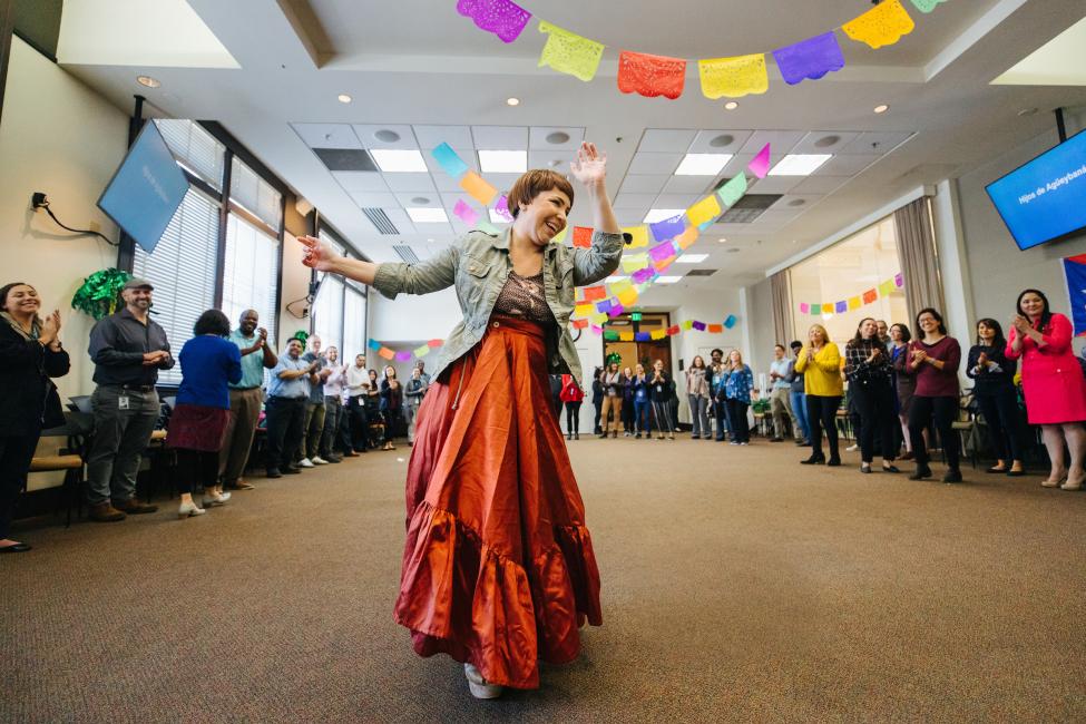 A woman in a long red skirt dances in a large room with colorful decorations hanging on the walls and from the ceiling.