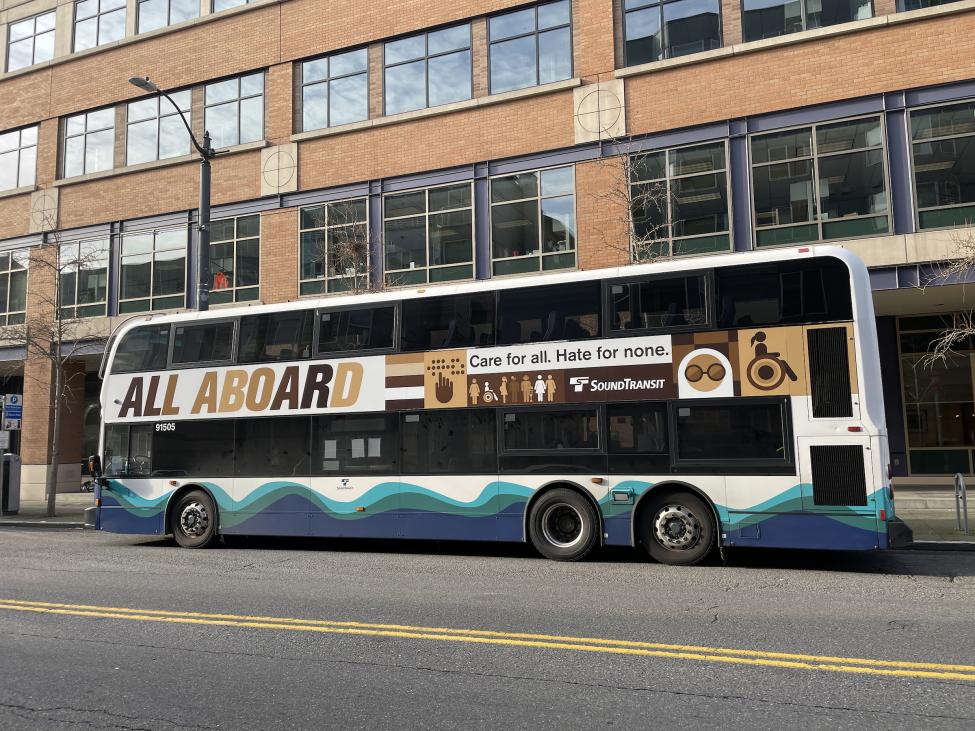 A Sound Transit double decker bus is wrapped in an advertisement stating "All Aboard. Care for All. Hate for none."