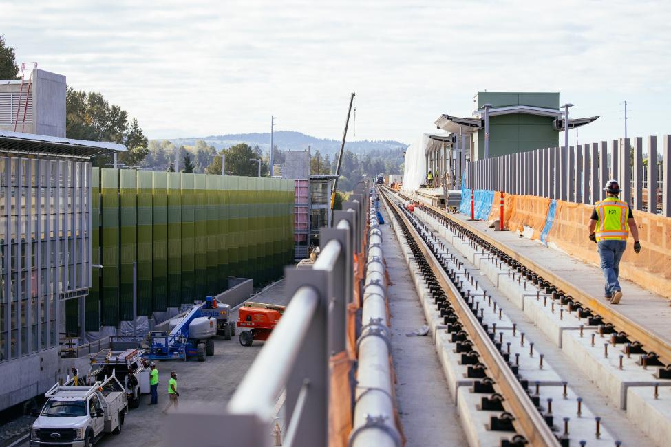 A construction worker walks along the platform at South Bellevue Station, with the parking garage visible on his left.