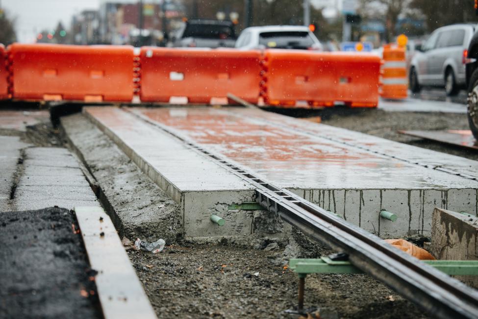 Rails can be seen coming out of concrete, with an orange construction barrier in the background.