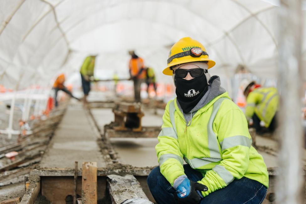 Cristina Tierce wears a yellow jacket, hard hat and face covering while working on the Hilltop Tacoma Link Extension.