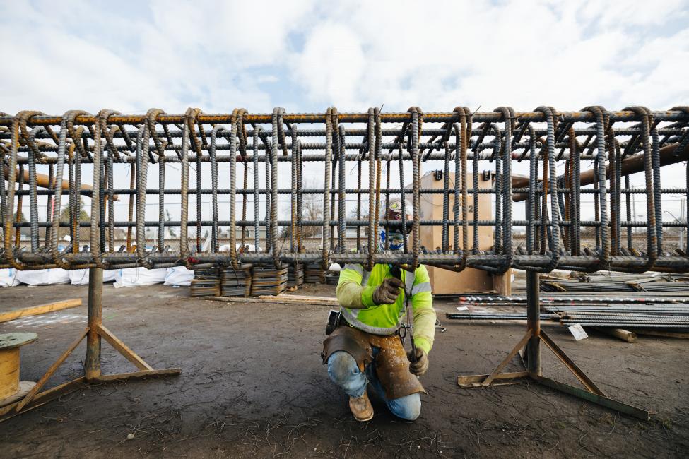 A worker kneels behind a rebar cage.