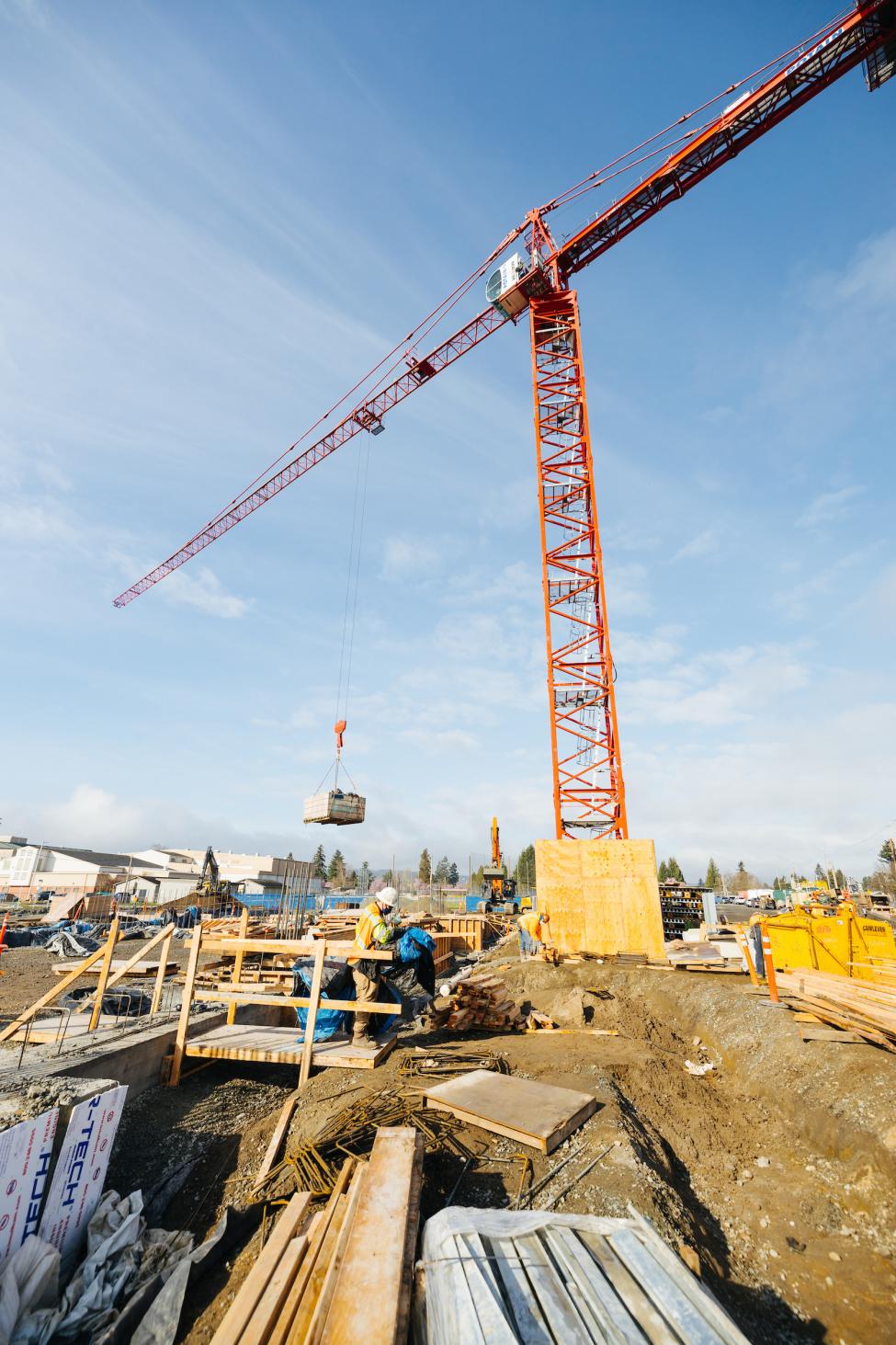 A large red crane lifts construction equipment into the air.