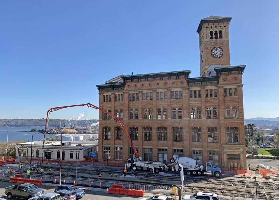 Photo of construction workers pouring and smoothing concrete for rails with Old City Hall and Port of Tacoma in Background, Hilltop Tacoma Link Extension