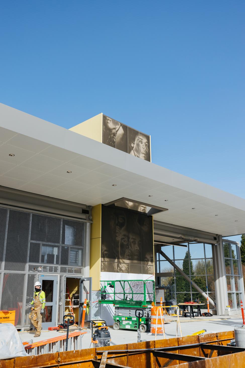 A mural features many faces of Jimi Hendrix. It is being installed at a light rail station under construction.