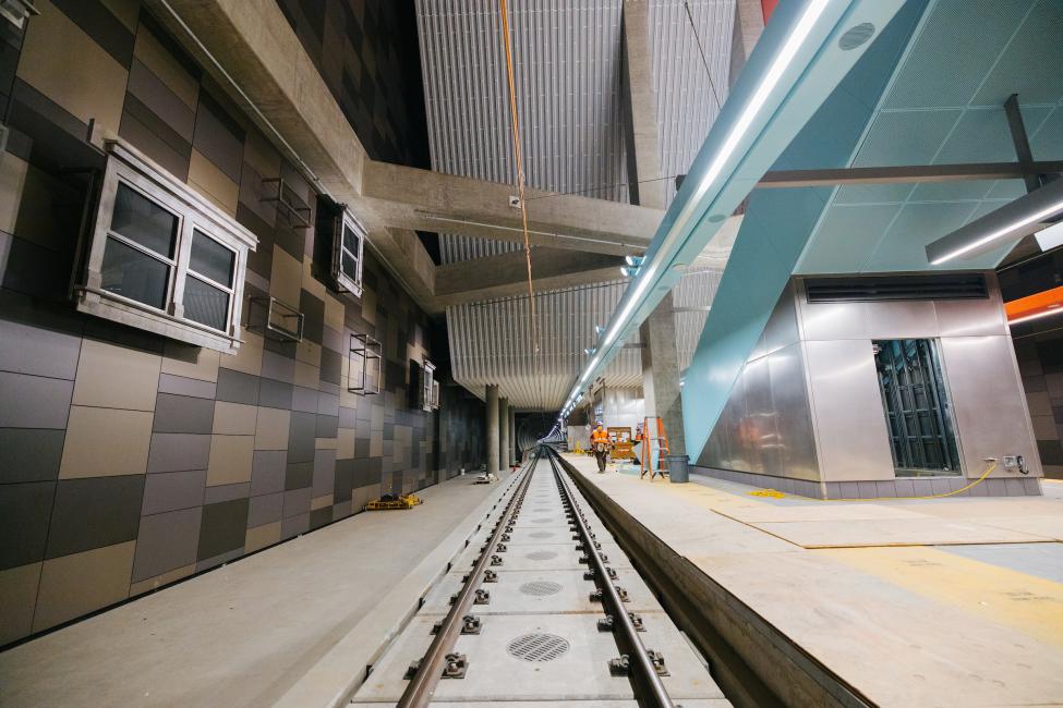 A view of U District Station from the train tracks. Gray and black paneling is visible on the wall to the right, and the platform is on the left.