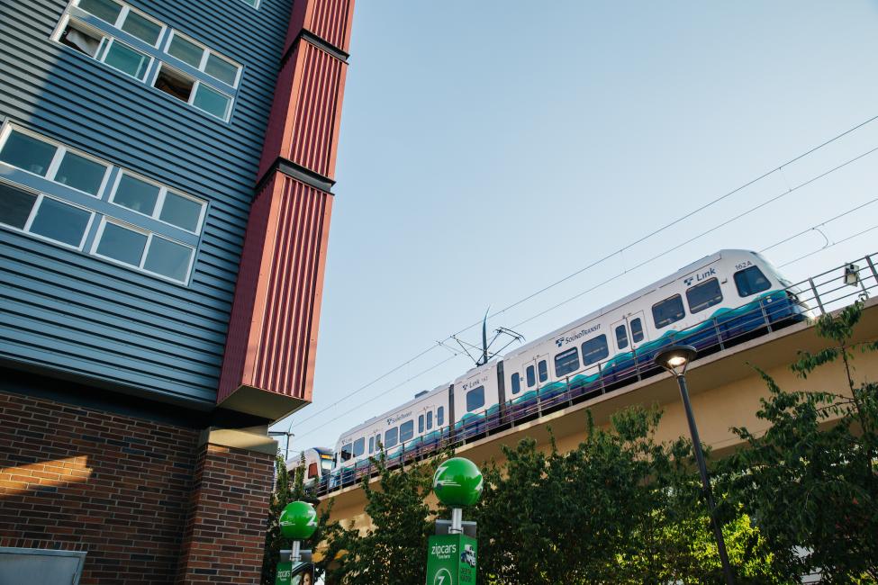 A light rail train runs on an elevated guideway next to an apartment building.