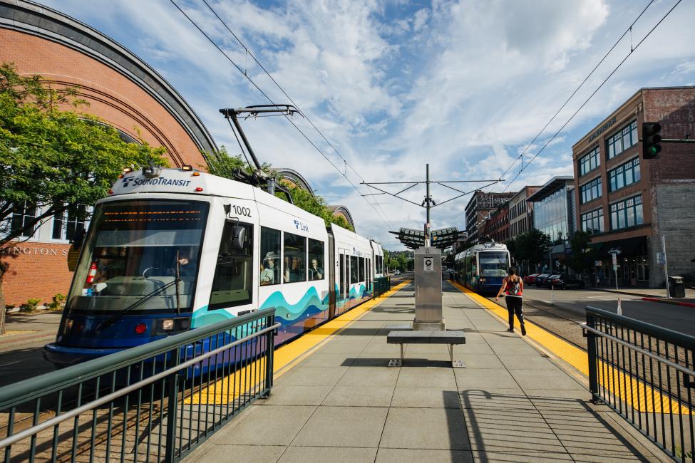 A Tacoma Link train pulls into a platform on a sunny day.