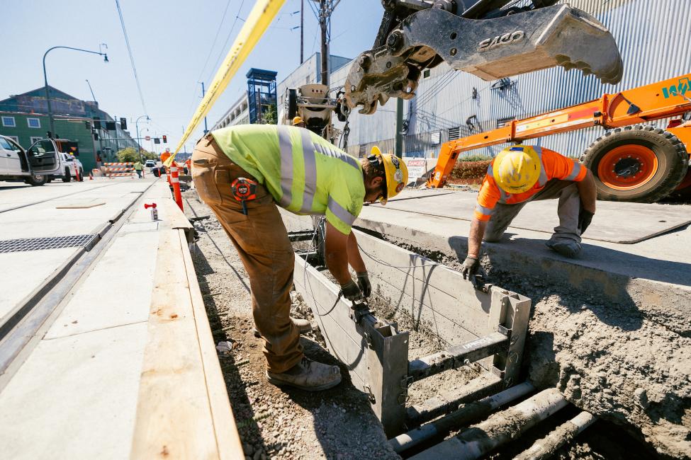 A construction worker kneels down to work on the light rail tracks.