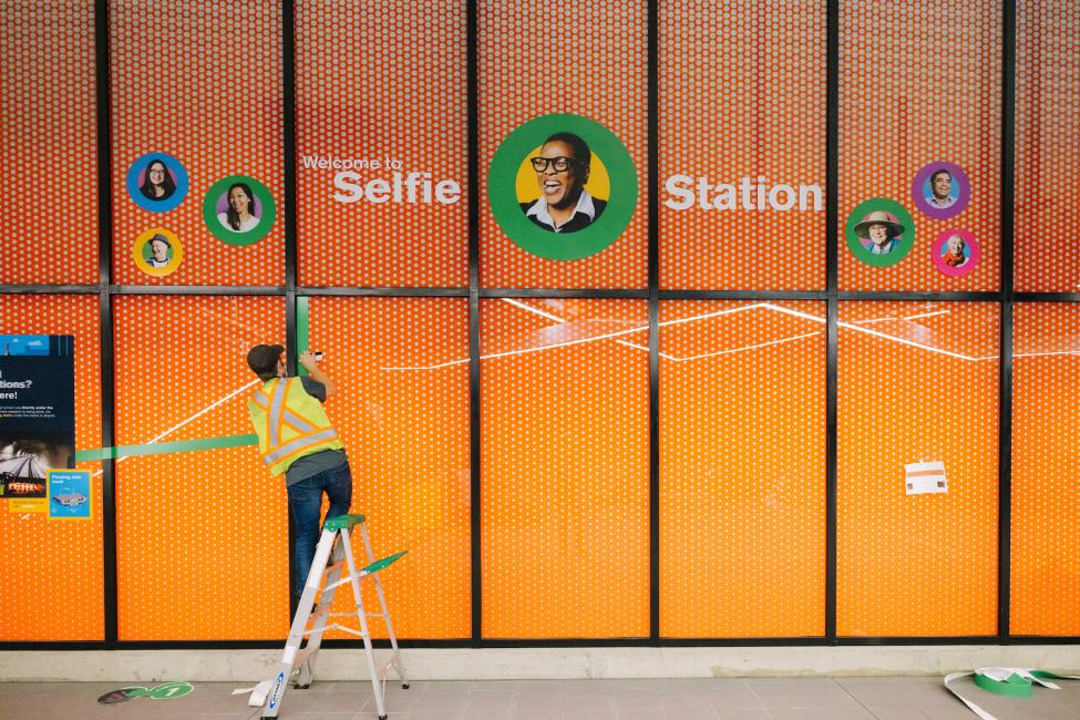 A colorful sign on an orange wall reads "selfie station."