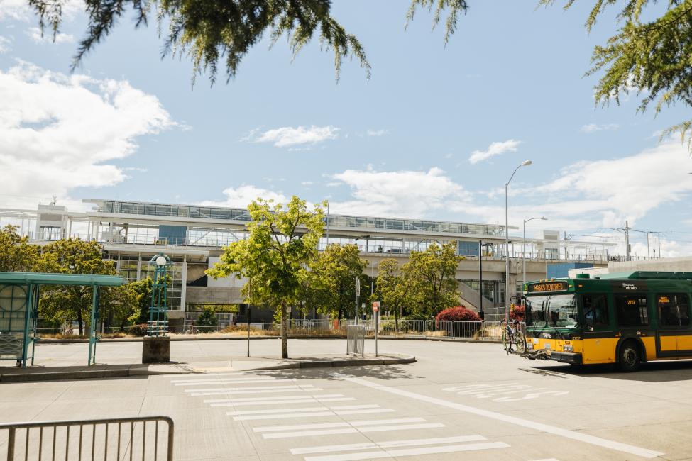 A King County Metro bus drives through the bay near the new Northgate light rail station on a sunny day. A train can be seen in the background.