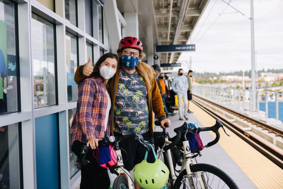 Two people smile with their bikes at the platform of Northgate Station.