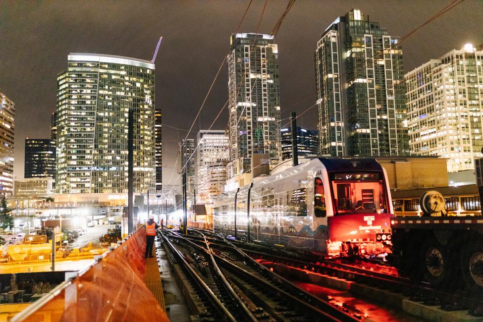 A link light rail train being pushed along the tracks just east of the Bellevue Downtown Station at night. 