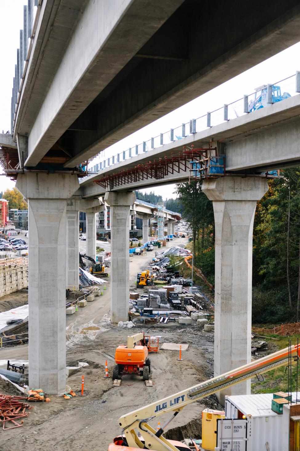 Girders in place for elevated light rail tracks, with construction equipment on the ground nearby.