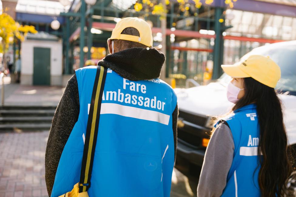 Two fare ambassadors wearing face masks talk to each other.