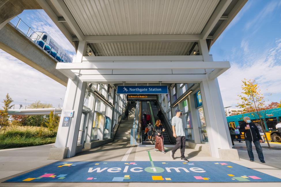 Riders pour through one of the Northgate Station entrances that features a giant "Welcome" matt on a sunny October day. 