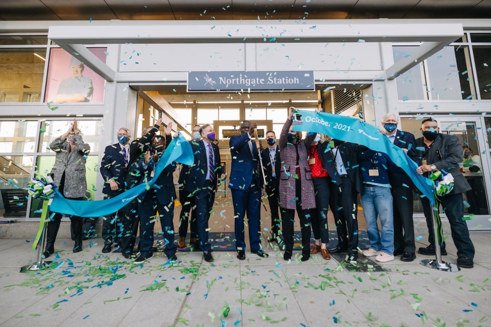 Photo of Sound Transit employees cutting a teal blue ribbon at Northgate Station opening for 1 Line, Northgate Link Extension