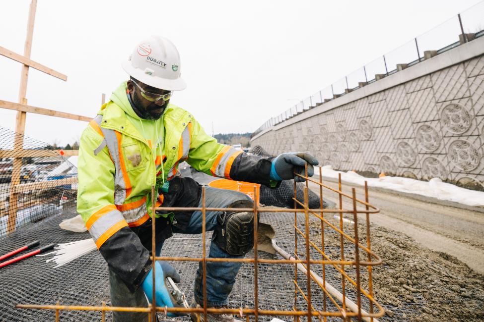 A worker in a yellow jacket and hard hart builds something on a construction site.