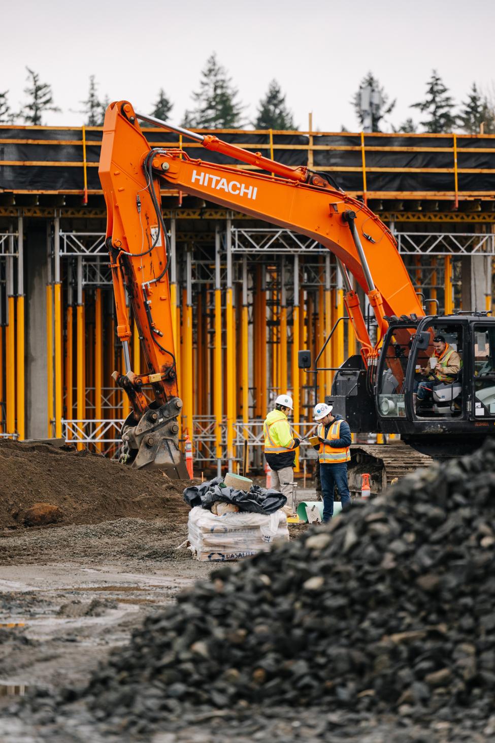 Orange construction equipment, with workers in the foreground and future light rail in the background.