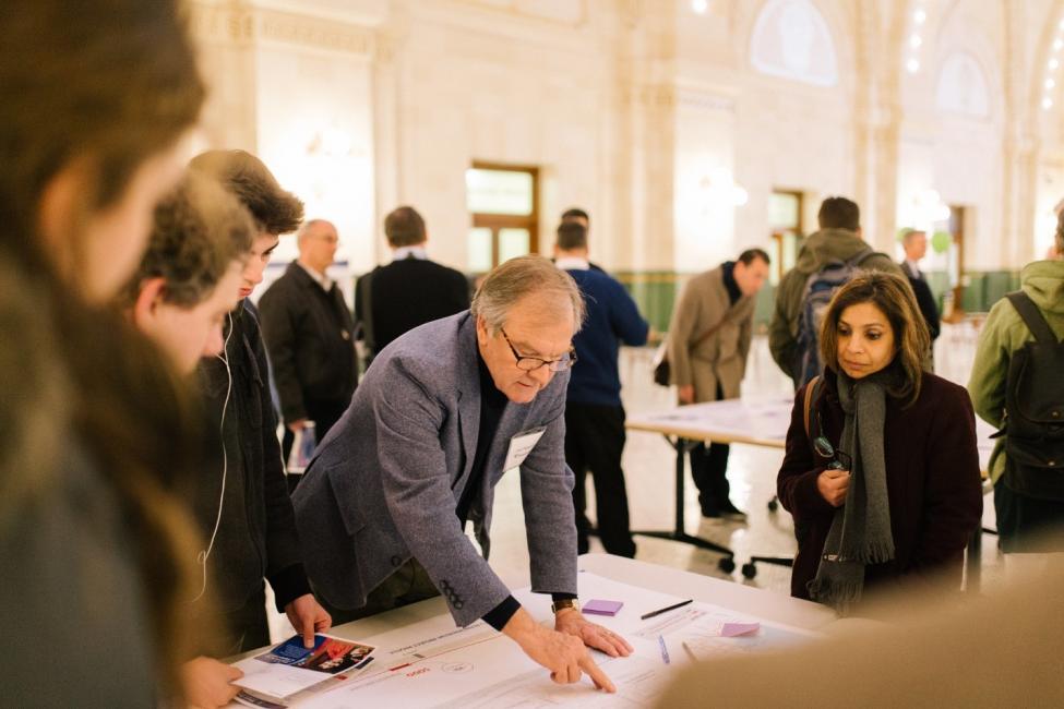 Community members learn more about the West Seattle/Ballard Link Extension project during a 2018 open house at Union Station where they gather around a man pointing out features on a large table-top map.