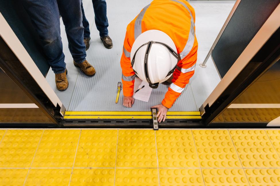 A person in a white hard hat and orange jacket kneels down to test something on a Link train. at the entrance 