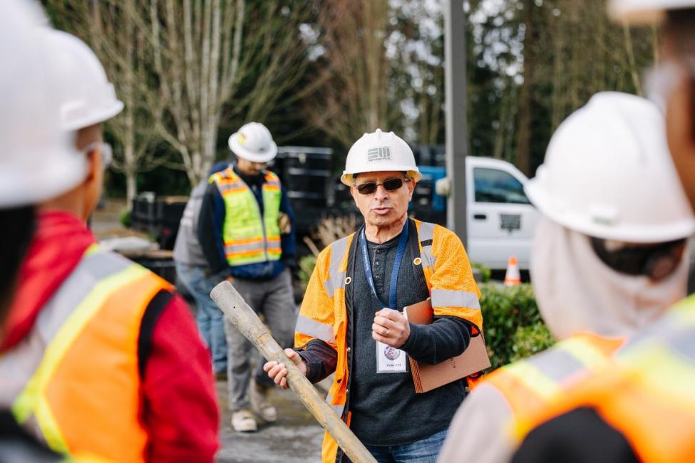 Hisham Sarieddine, wearing a hard hat and orange vest, talks to people also dressed in protective gear. 