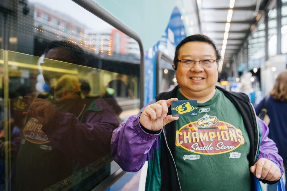 A person wearing a Seattle Storm T-shirt holds up a Storm ORCA card.