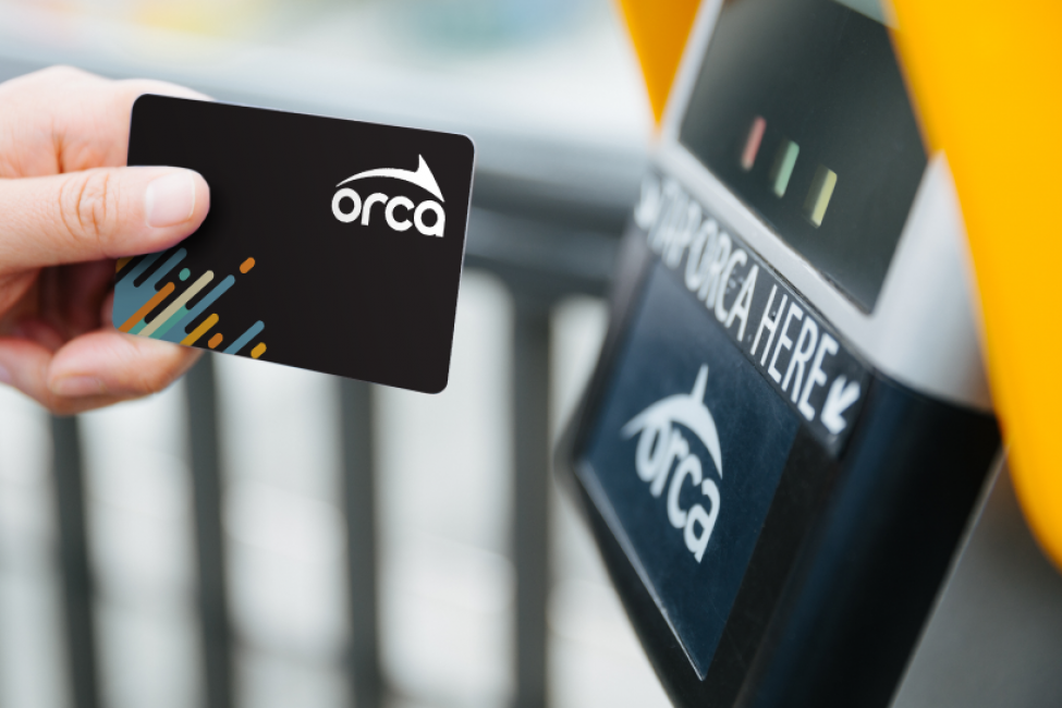 A hand reaches out to tap a black ORCA card on a yellow reader.