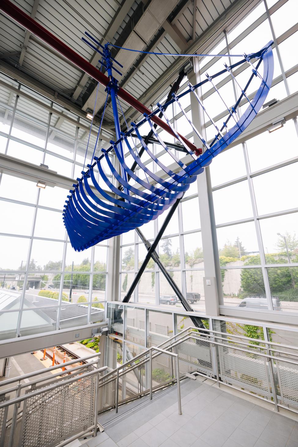 A blue sculpture is suspended in Mercer Island Station. It looks like a rowboat.