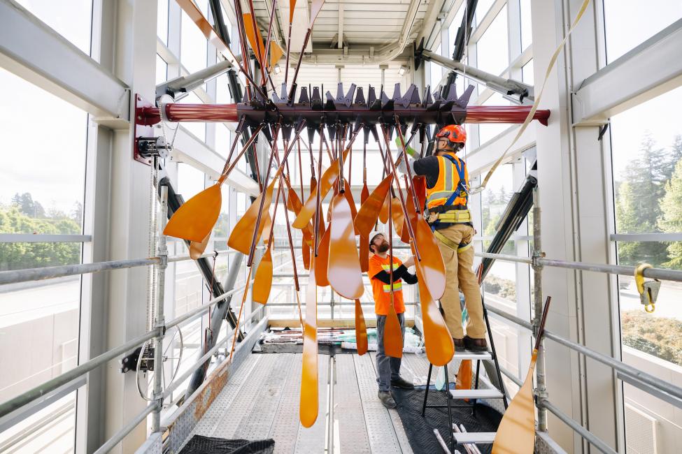 Workers install a sculpture of orange oars at Mercer Island Station.