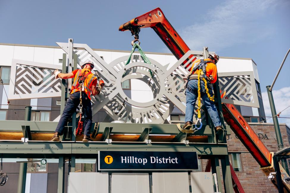Workers install sculptures on top of the new Hilltop District station.