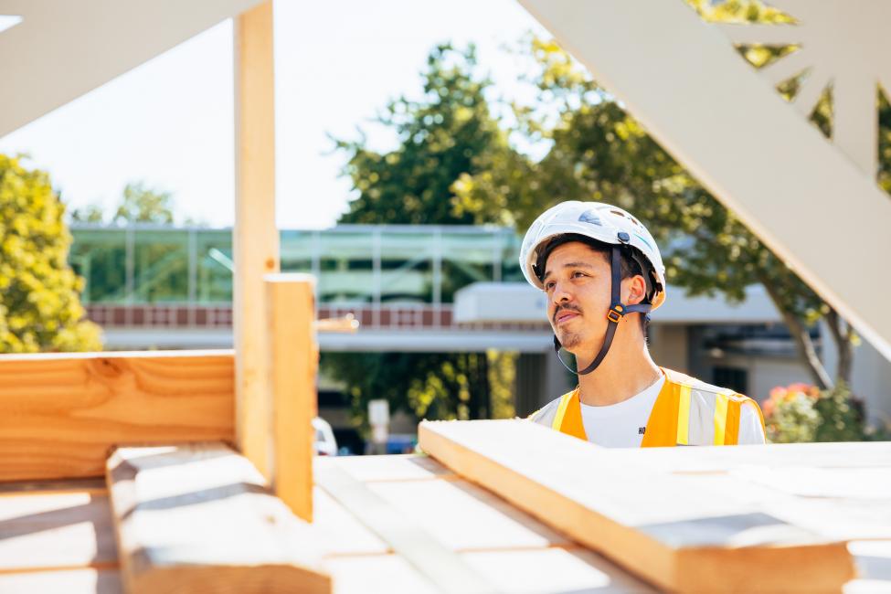 Kenji Stoll wears a hard hat and looks on as construction crews install his art.