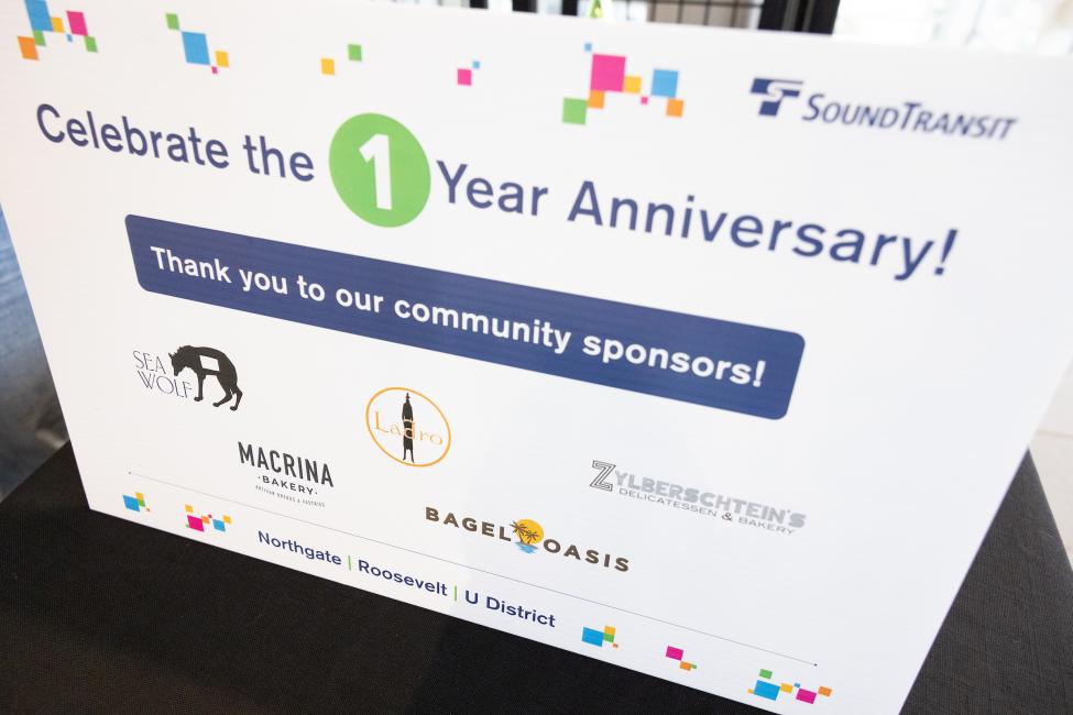 A sign says 'Celebrating the 1 line anniversary' and shows the event sponsor logos. 