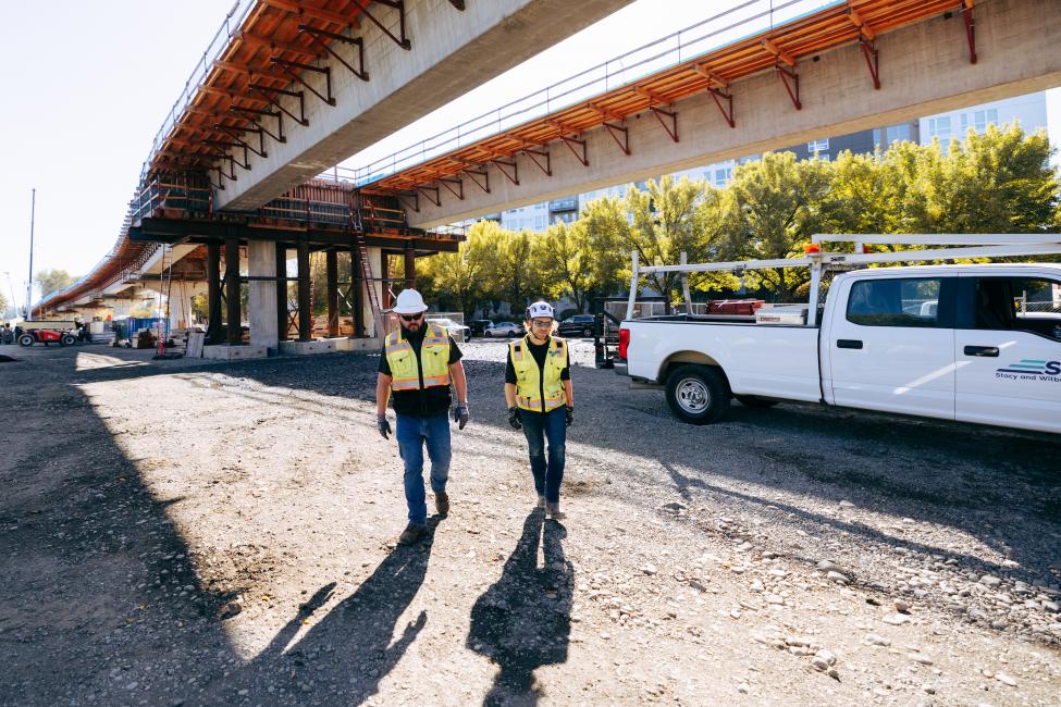 Two workers walk underneath an elevated guideway under construction. 