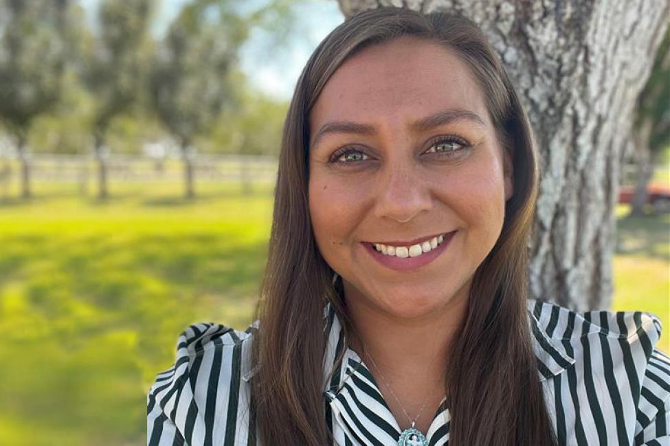 Valerie Valero smiles while wearing a striped shirt, with trees in the background. 