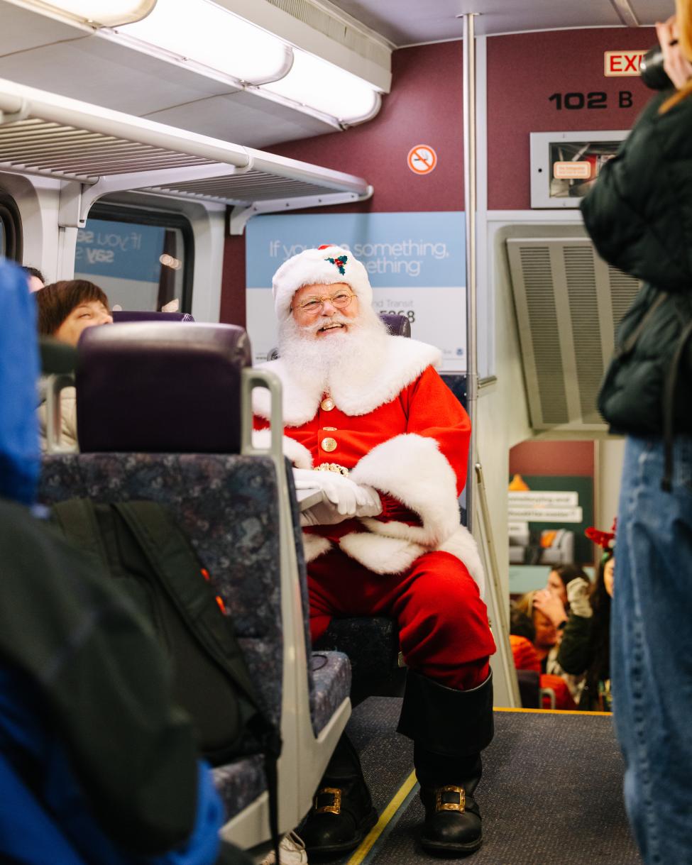 A person dressed as Santa Claus smiles while onboard a Sounder train. 