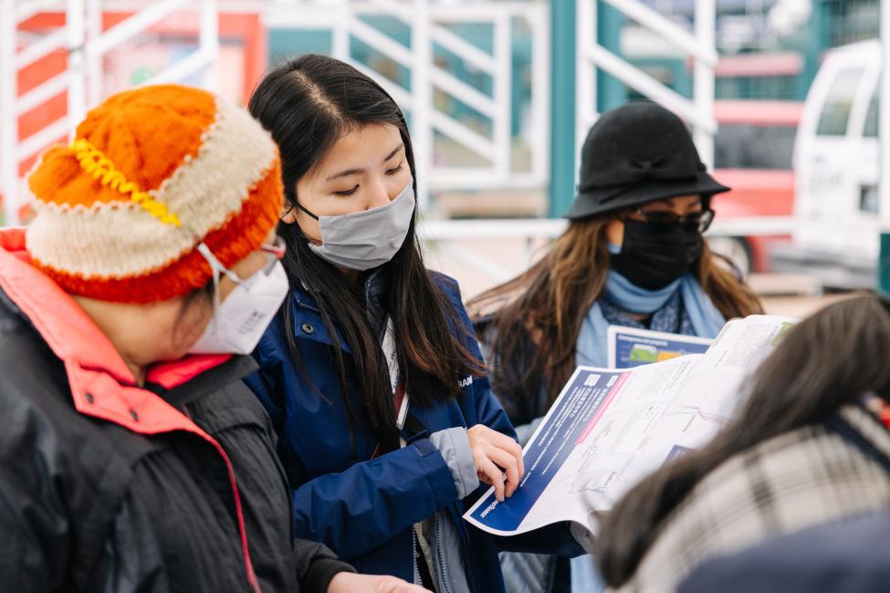 A woman in a face mask talks to another woman and explains something on a piece of paper. 