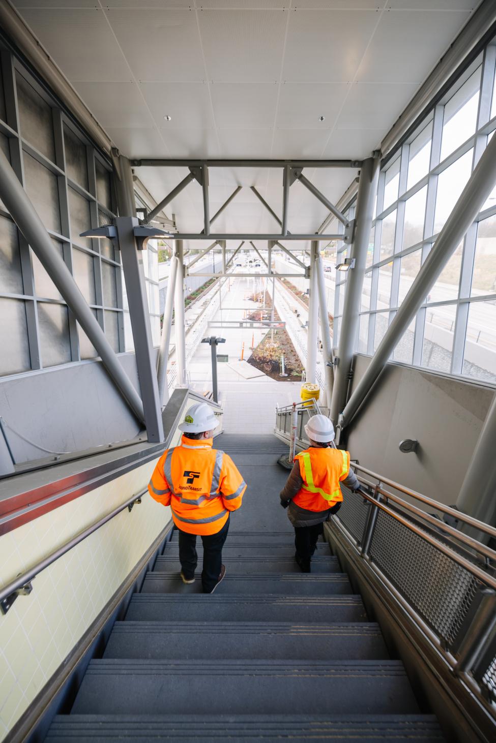 Barbara Thomas and a Sound Transit employee walk down the stairs to the Judkins Park Station platform. 
