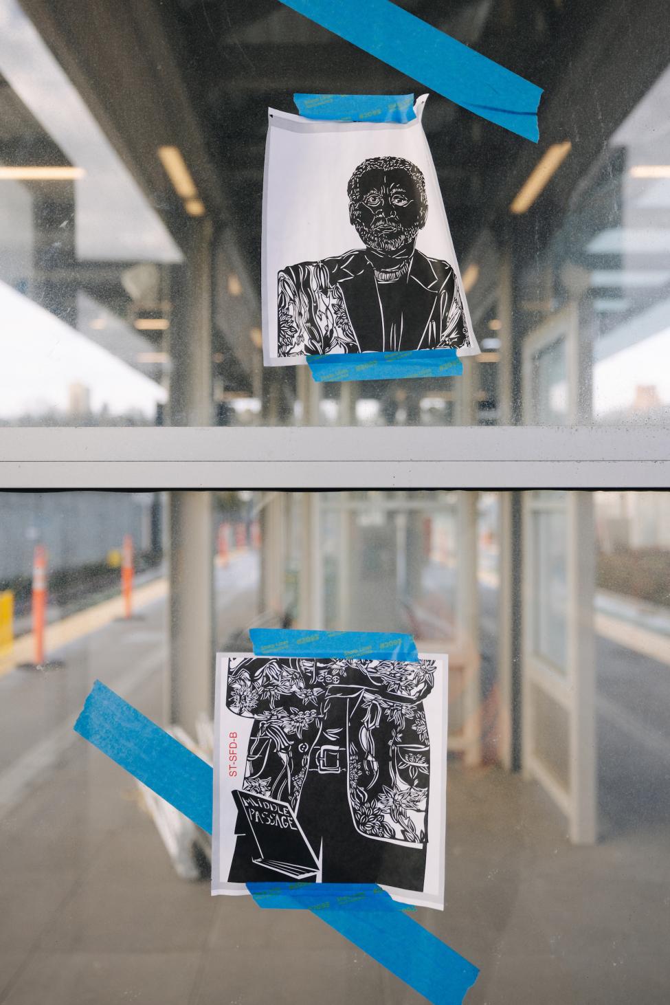 Concept art by Barbara Earl Thomas is taped to the glass of a windscreen on a light rail station platform. 