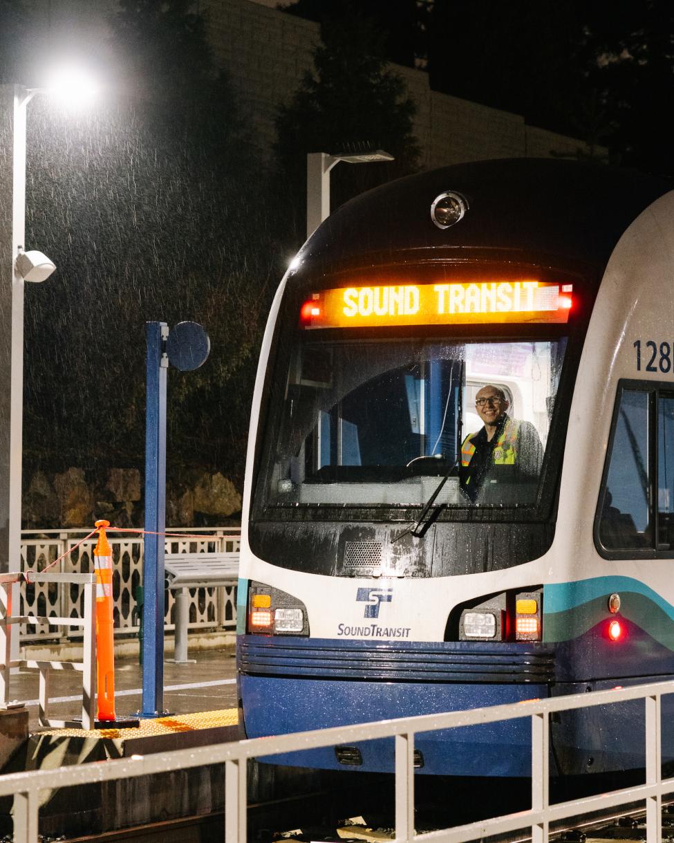 The front of a Link train, with an operator smiling at the camera inside the cab.