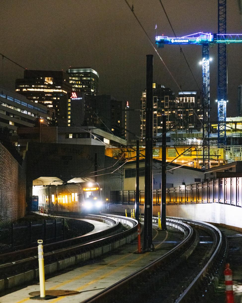 A train comes out of a tunnel at night, with downtown Bellevue lit up in the background.